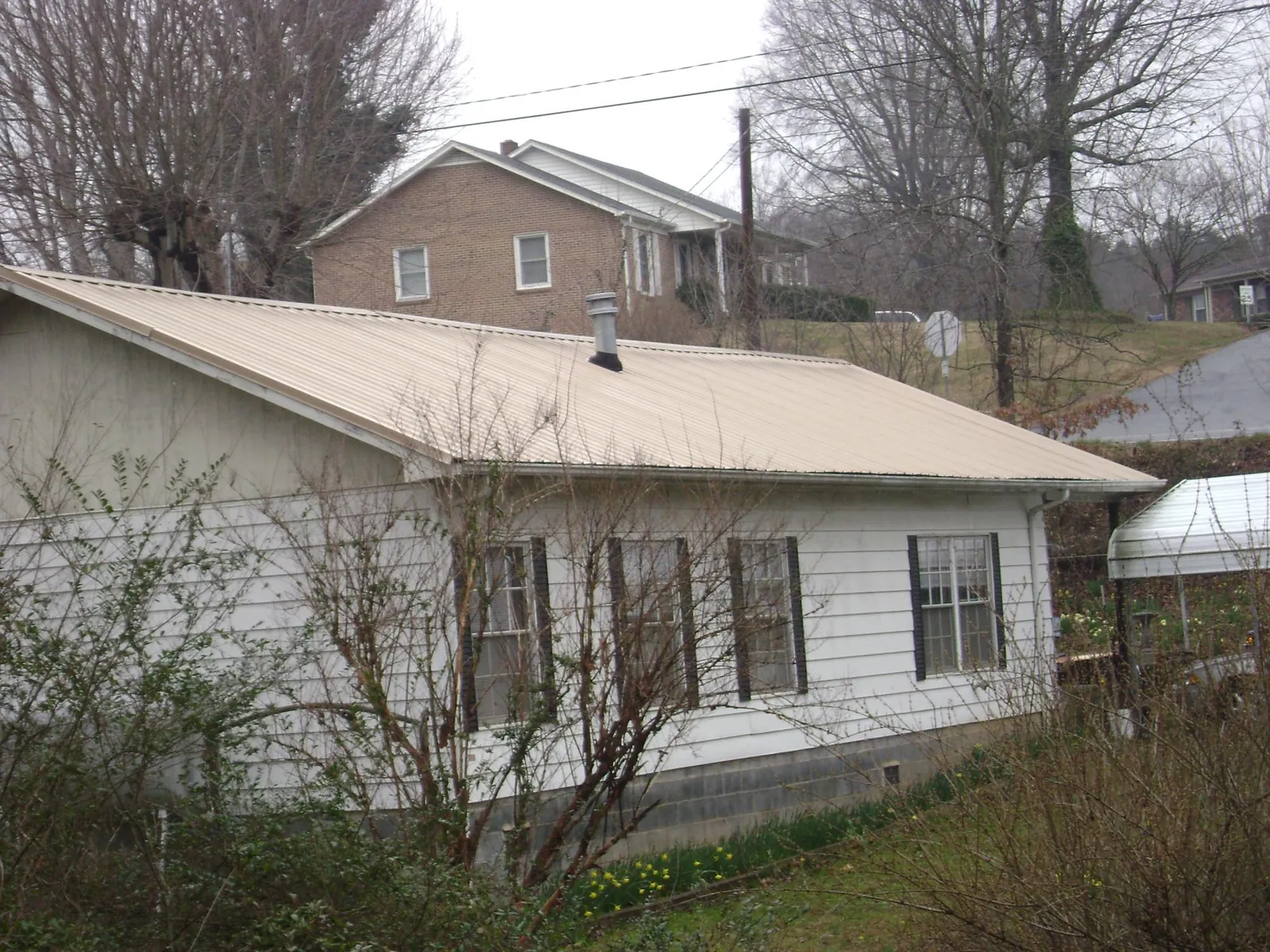 Tan metal roof on a white sided house set into a hillside — Commercial Roofing by Roofing Brothers in Halifax